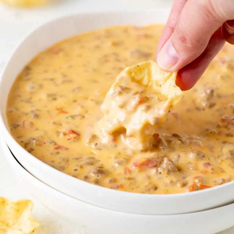 Chip dipping into a bowl of beef and sausage dip.