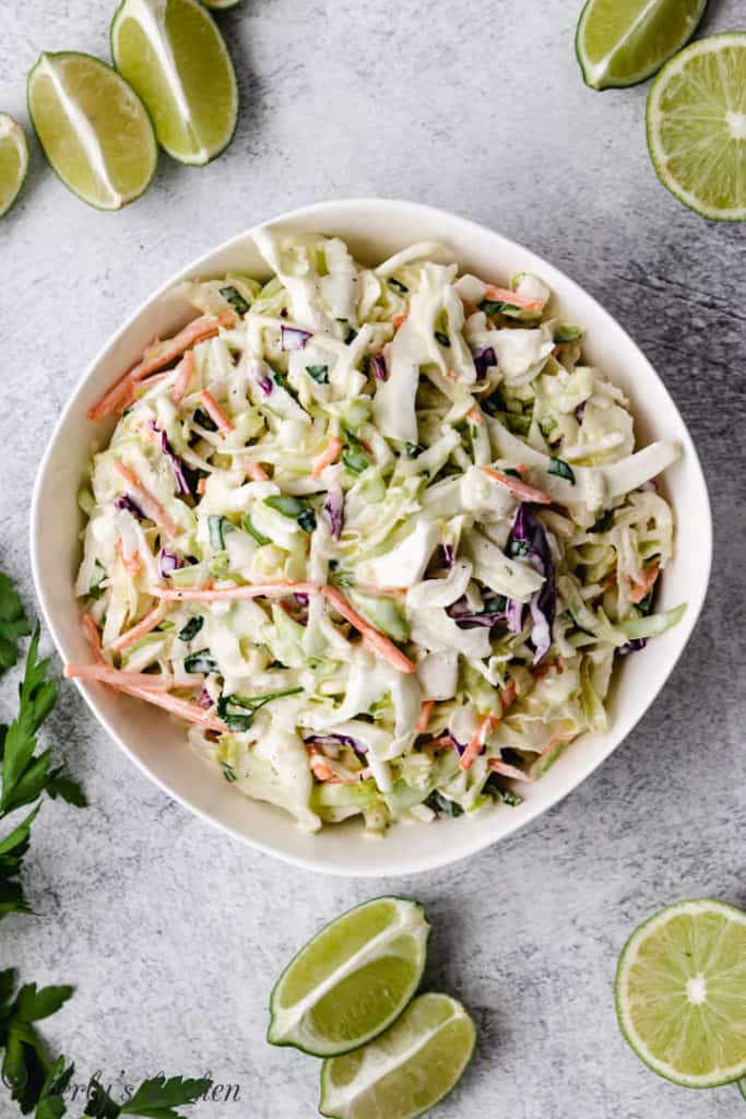 Lime wedges next to a bowl of coleslaw.