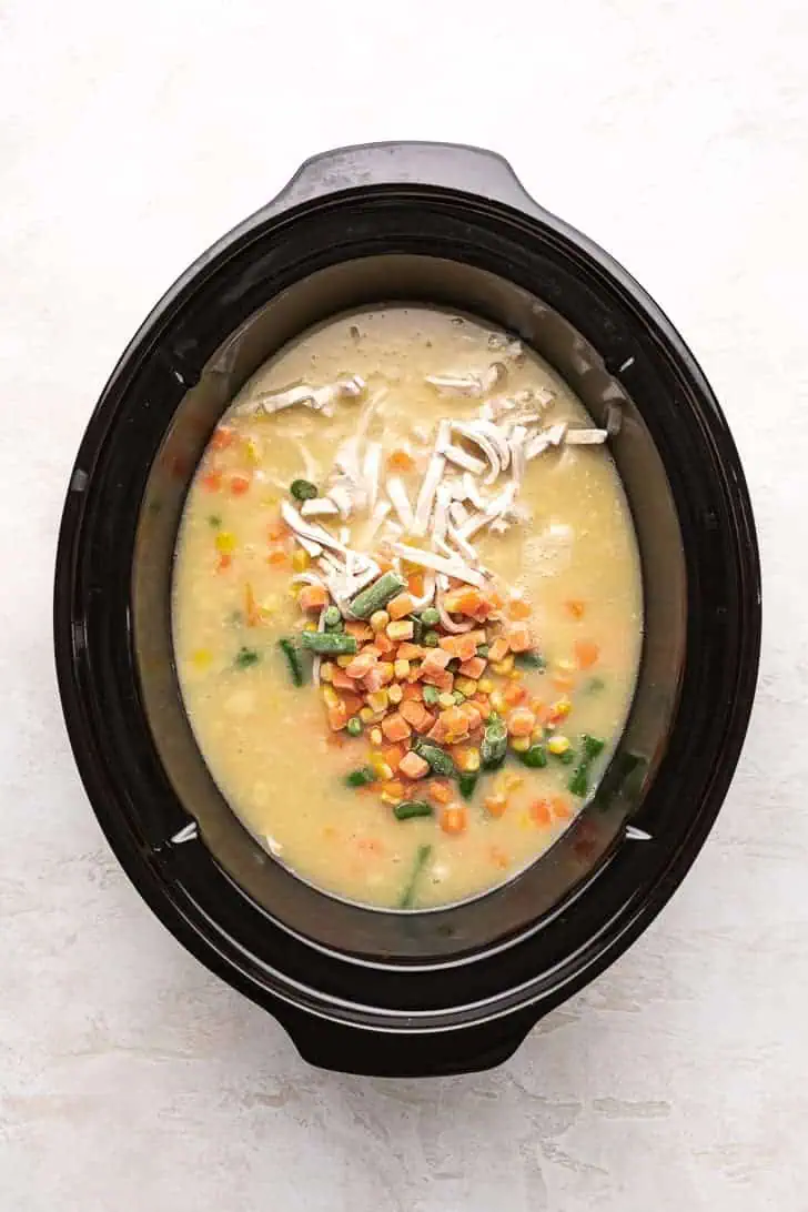 Frozen egg noodles and vegetables added to a crock pot.