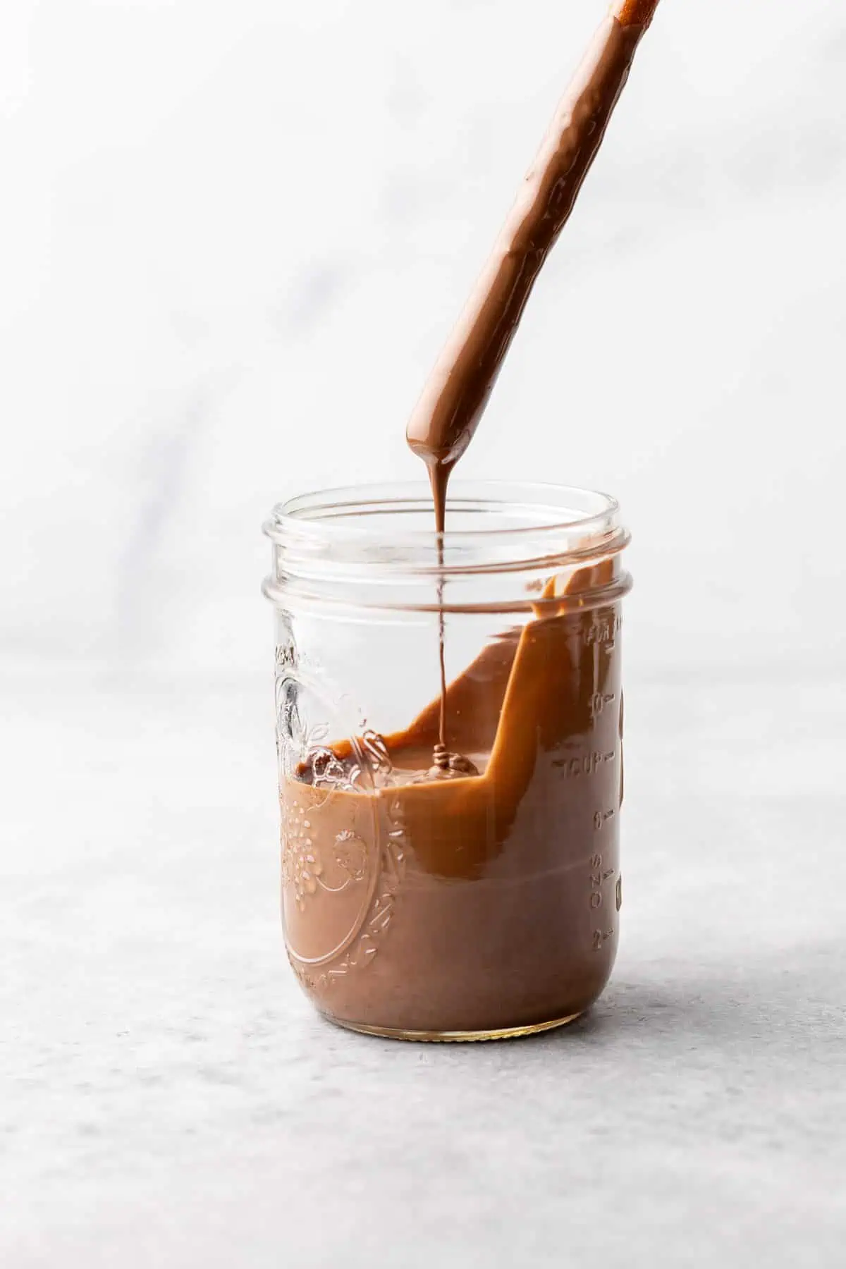 Chocolate dipped pretzel being held above a jar.