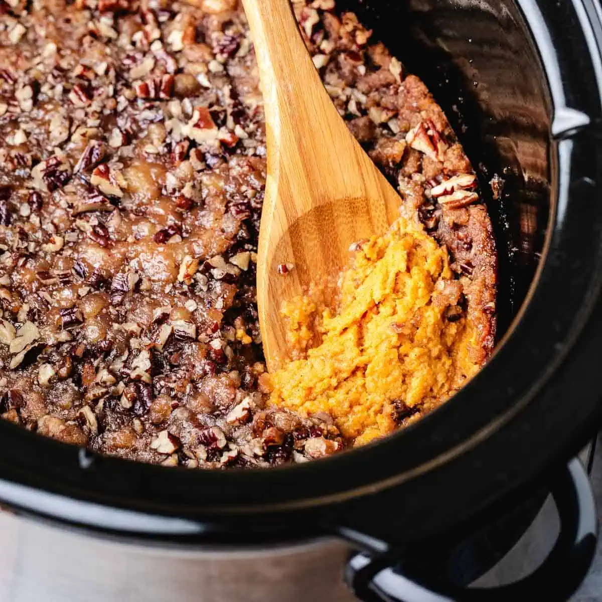 Close up view of a wooden spoon scooping sweet potato casserole.