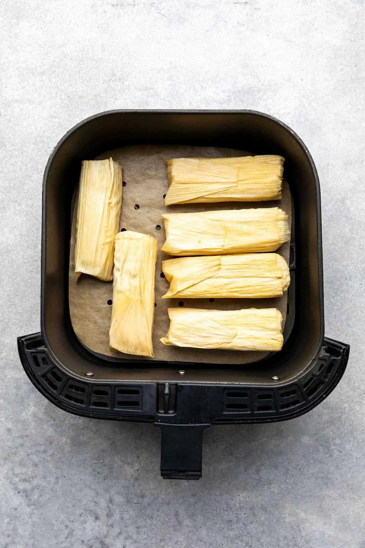 Frozen tamales placed in an air fryer basket.