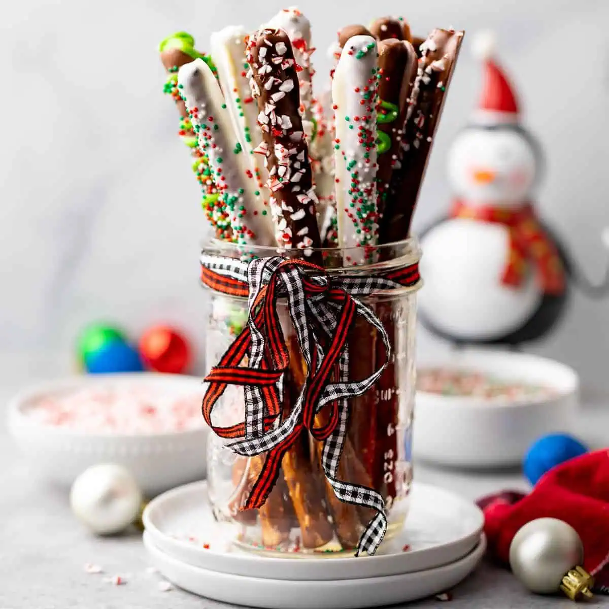 Mason jar with a ribbon filled with chocolate dipped pretzel rods.