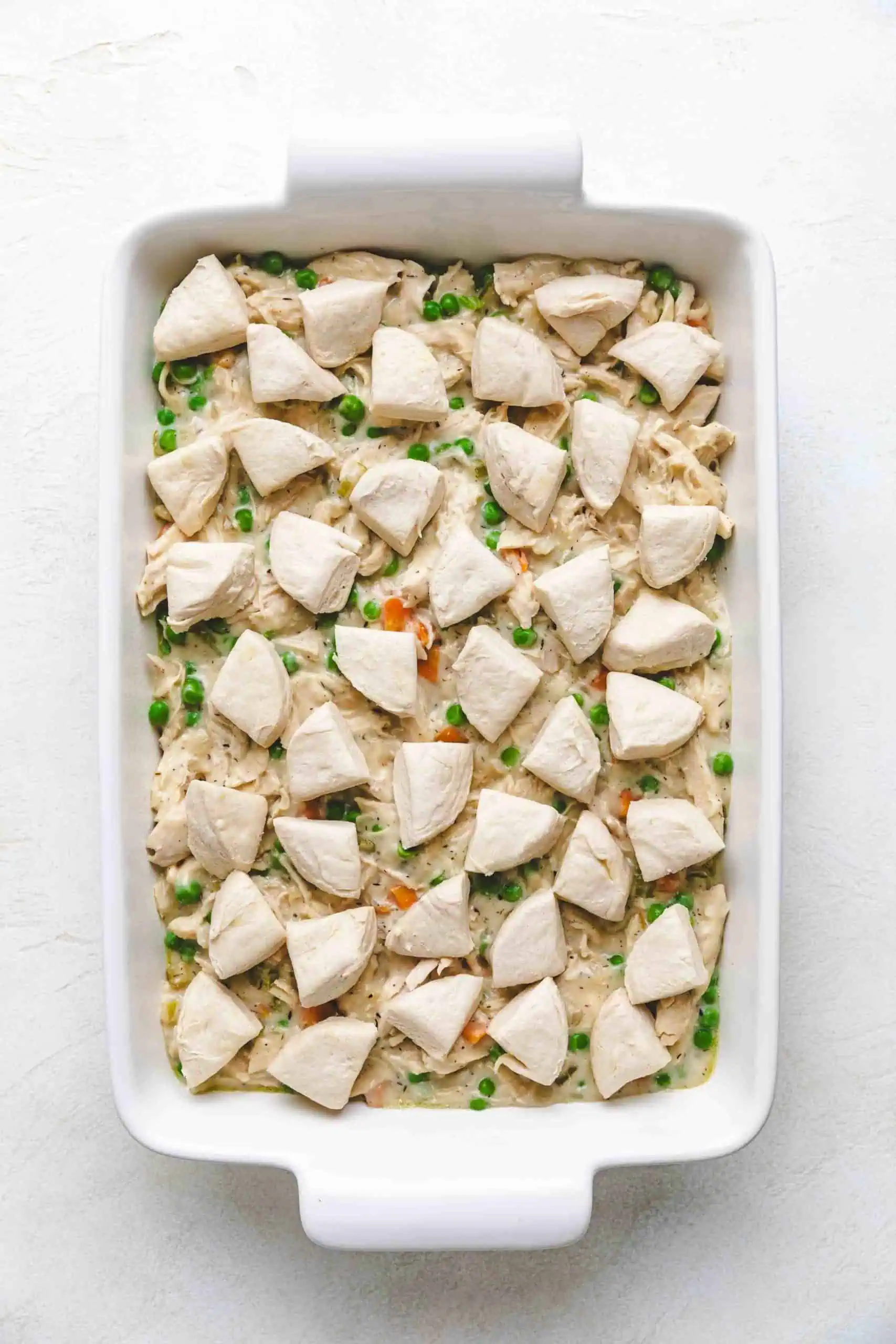 Unbaked chicken filling and biscuits in a baking dish.