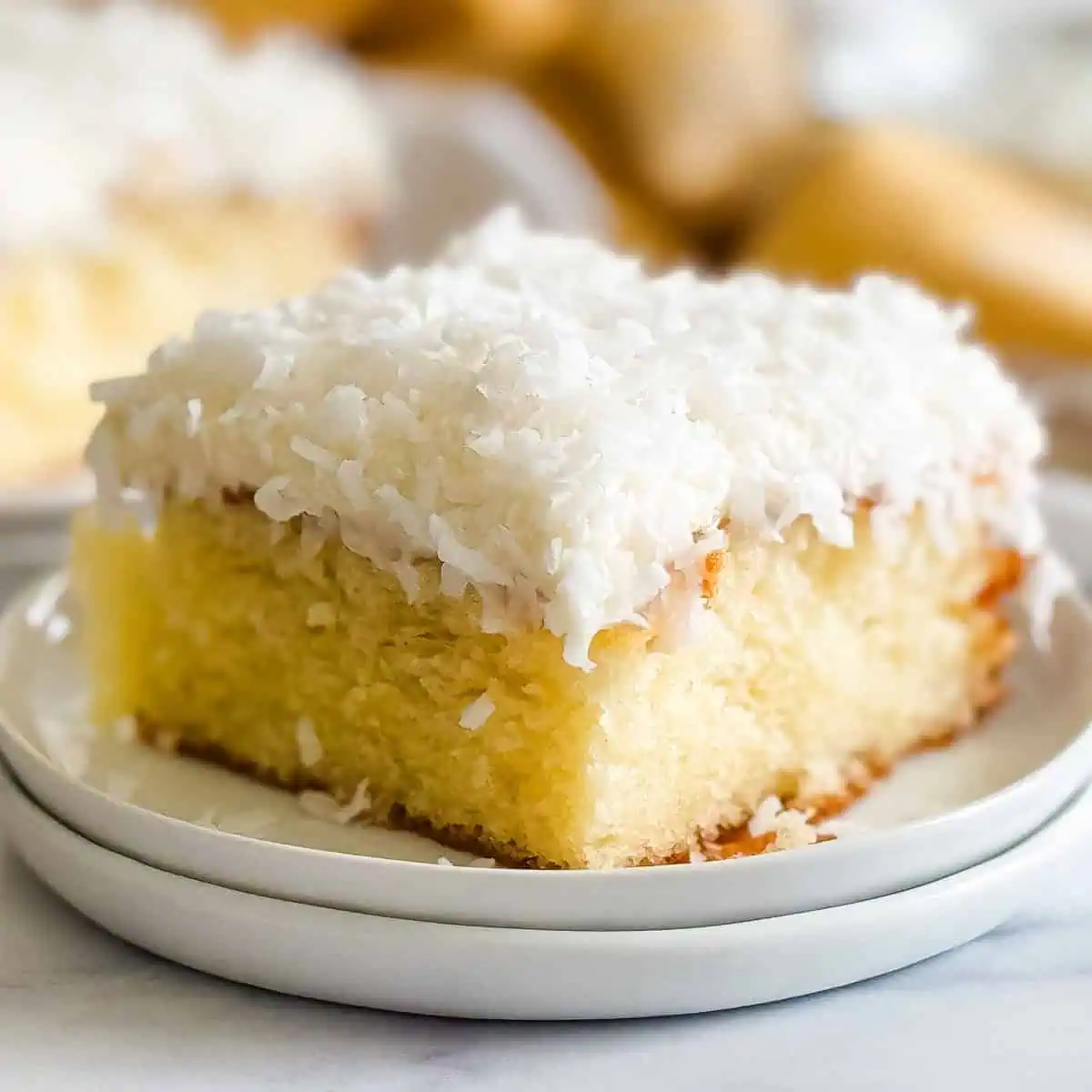 Slide of cake on a plate with coconut cream cheese frosting.