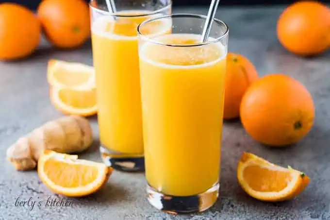 Fizzy orange drinks next to fresh oranges.