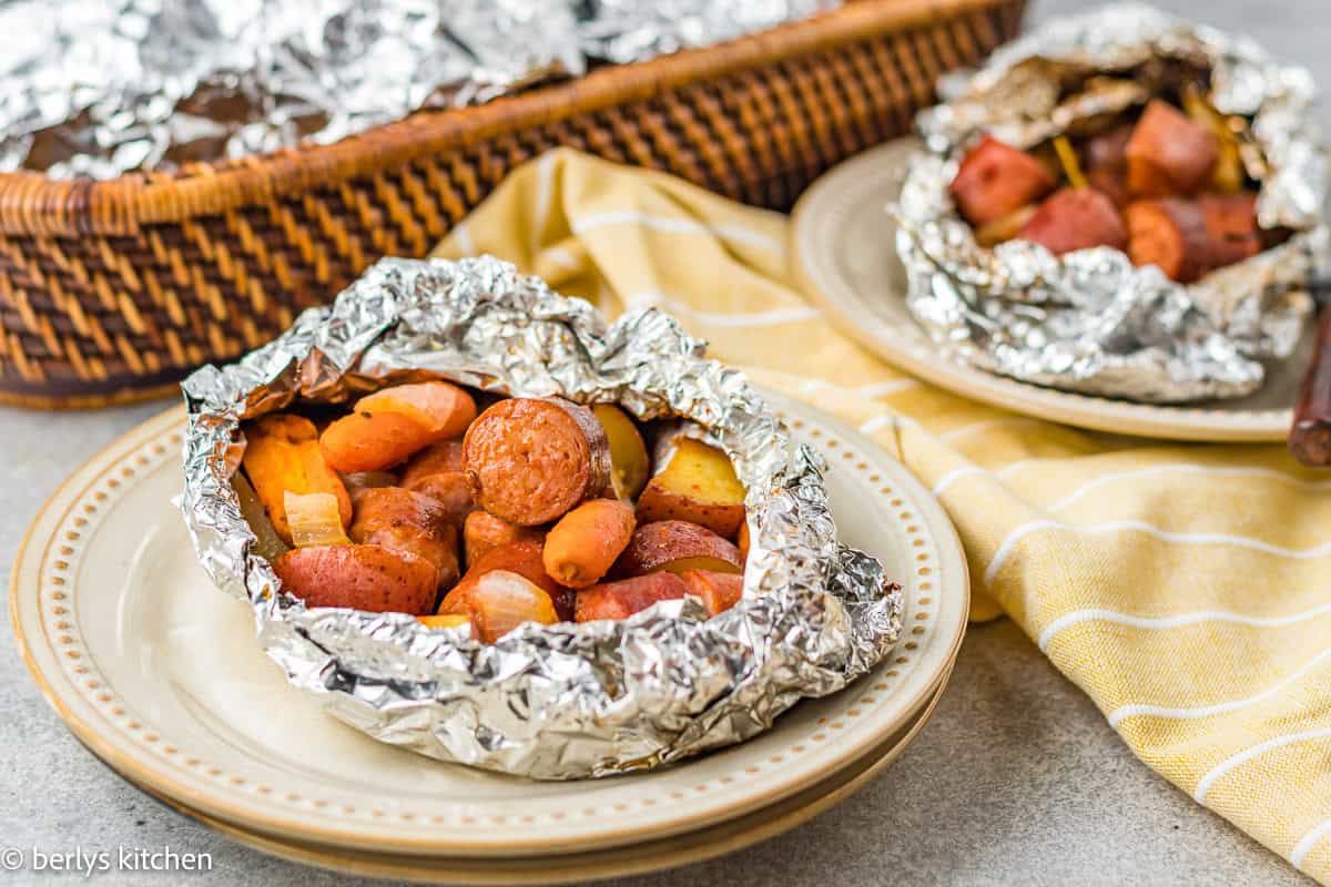 Sausage, potato, and carrots foil packet on a plate.