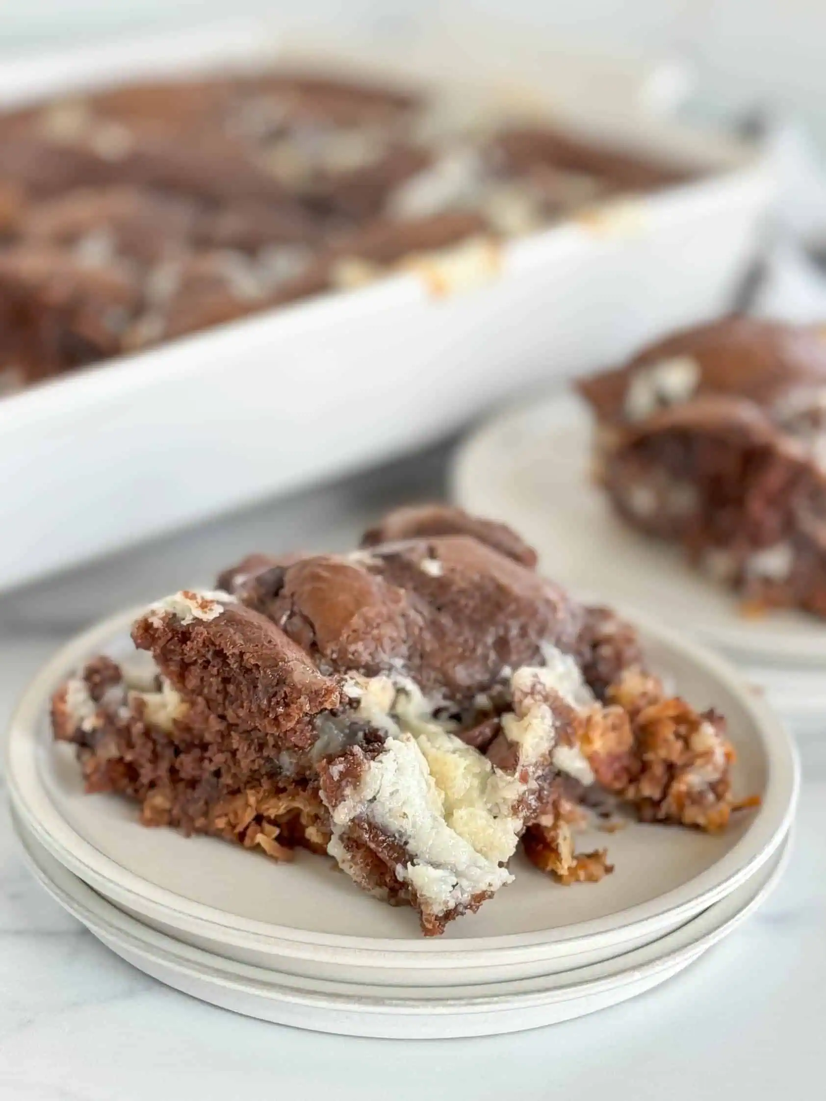 Scoop of german chocolate earthquake cake on a stack of gray plates.