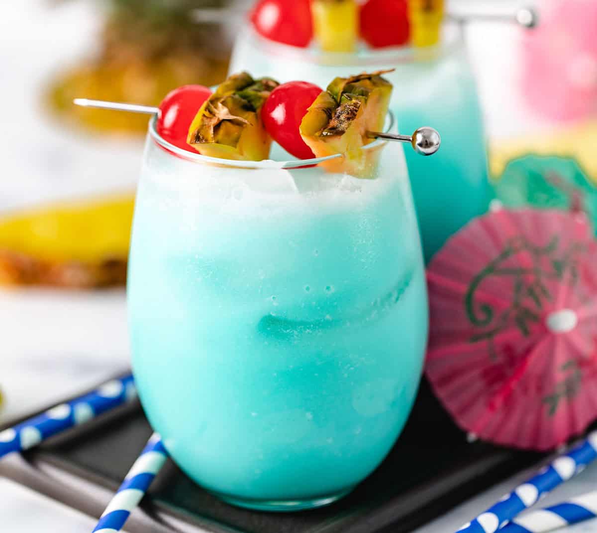 Blue cocktail with pineapple and cherries.