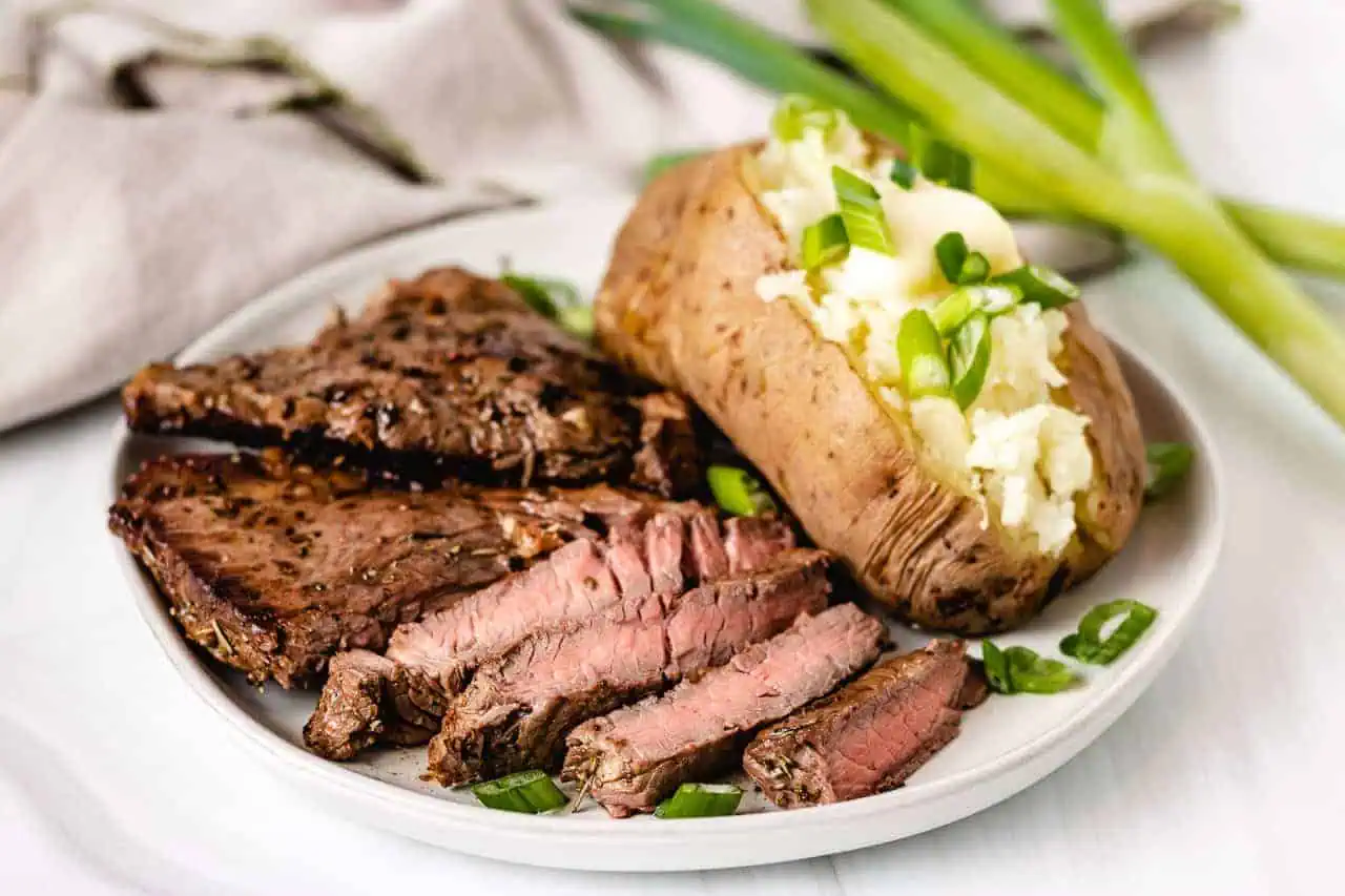 Sliced sirloin steak with a baked potato with butter.