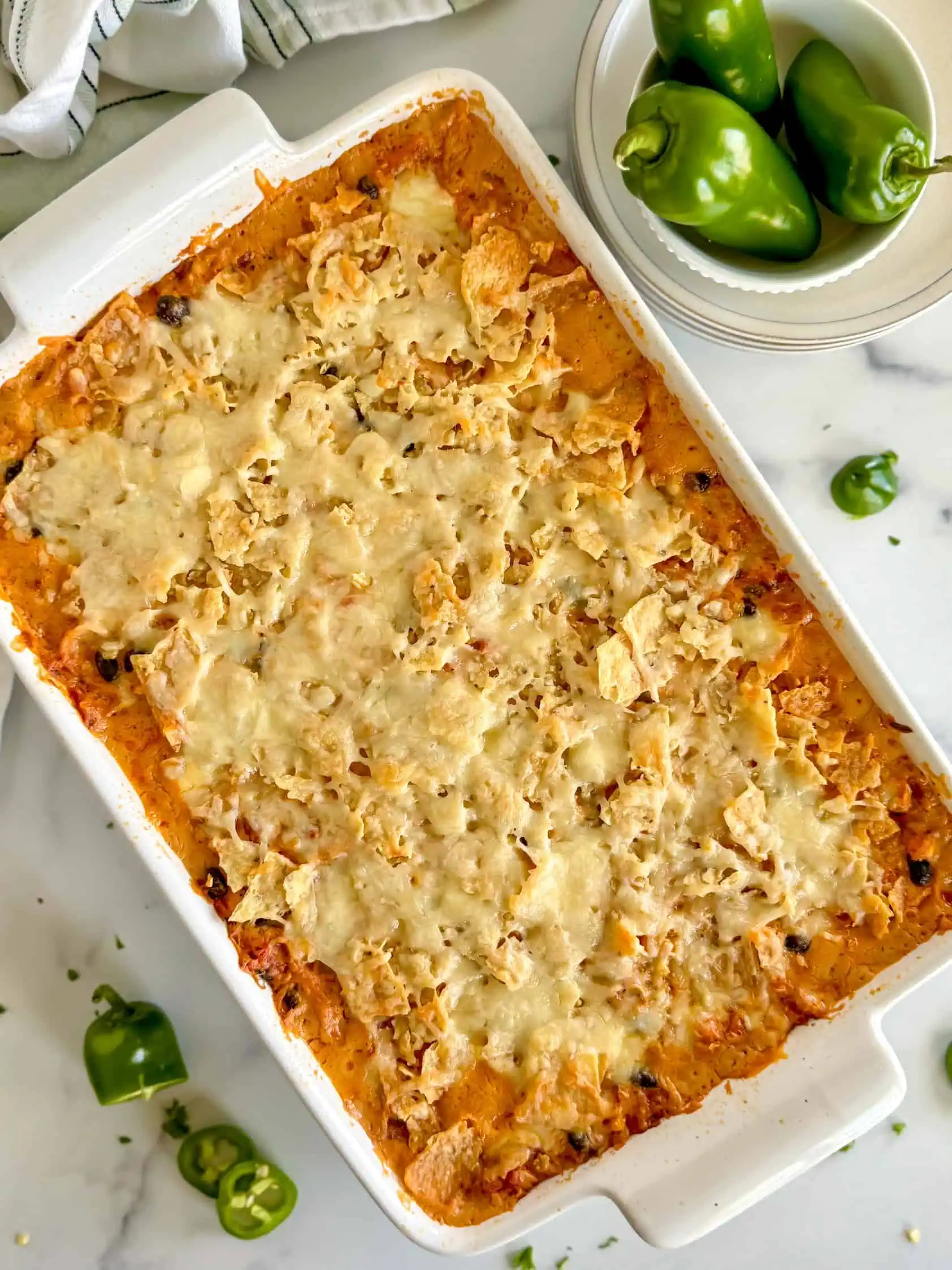 A top-down view of the creamy chicken taco casserole in a 9x13-inch baking dish, with sliced jalapeños nearby for garnish.