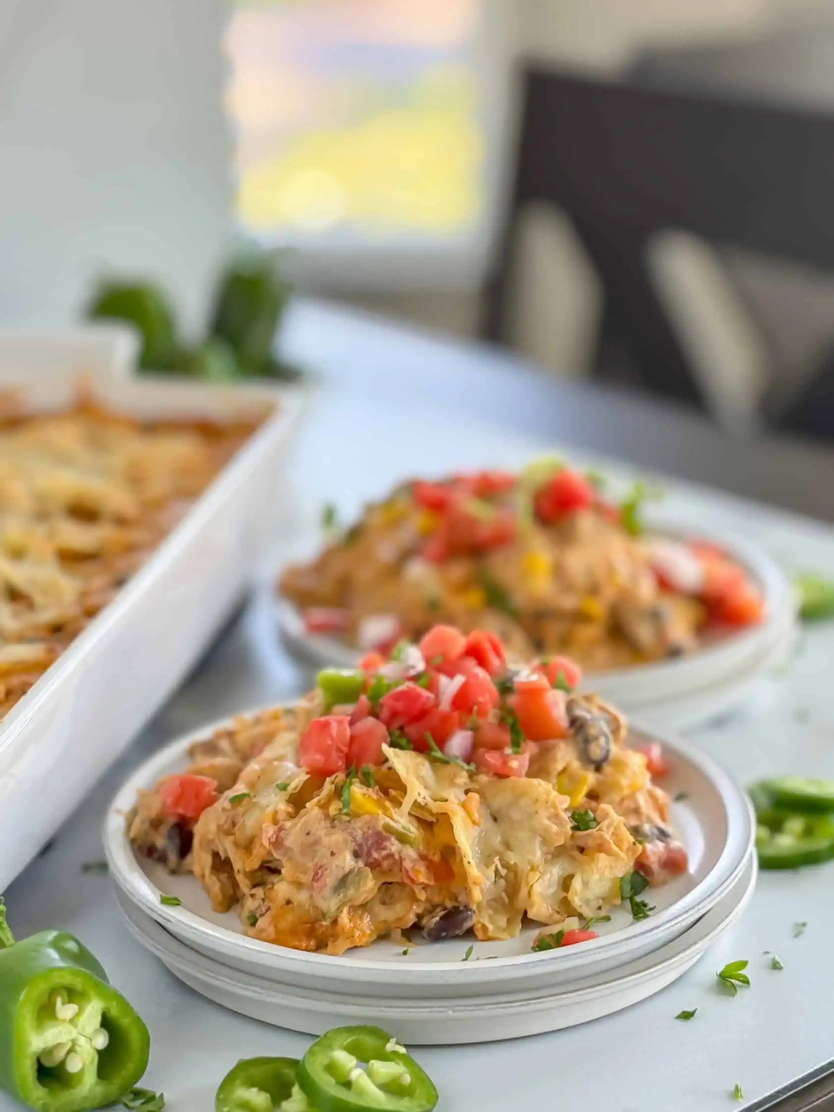 A slightly blurred background showcasing a serving of chicken casserole with diced tomatoes and chopped cilantro on a white plate.