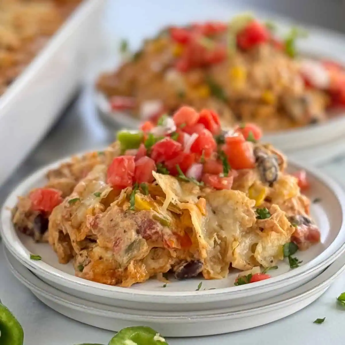 A close-up of a serving of taco casserole topped with diced tomatoes and chopped cilantro on a white plate.