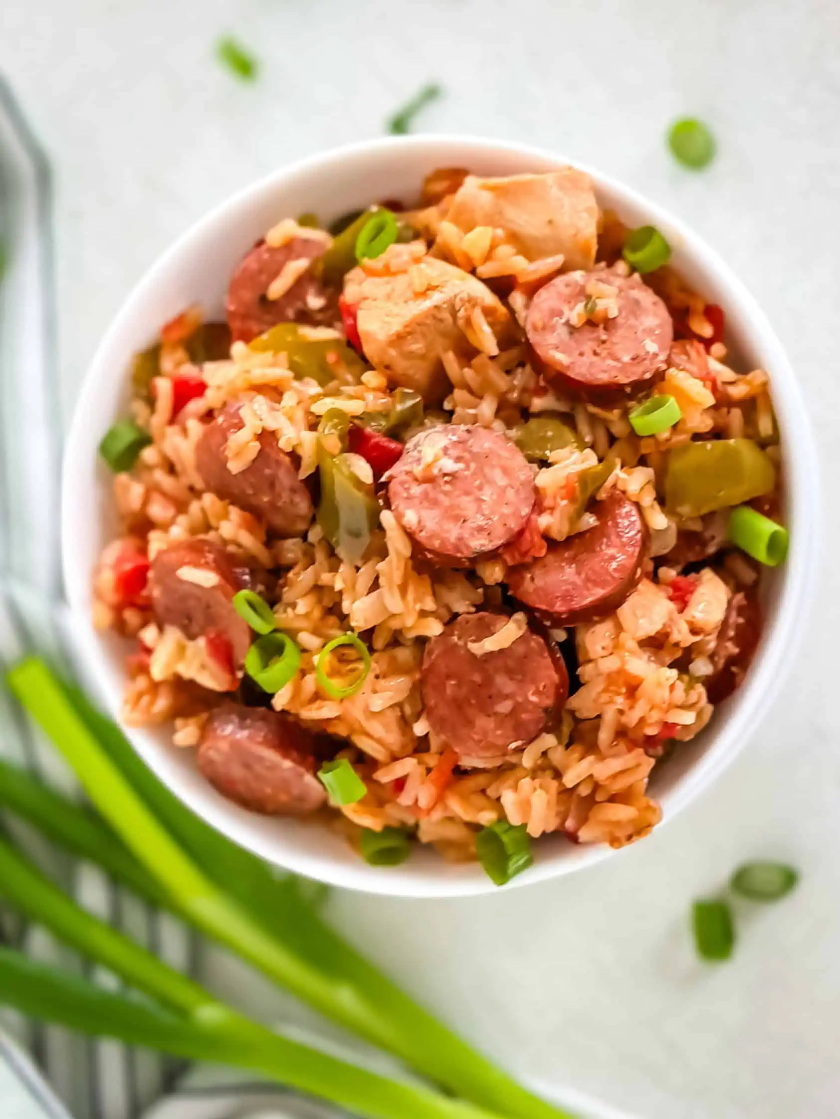 Overhead shot of a hearty rice and sausage dish, garnished with green onions, served in a white bowl.