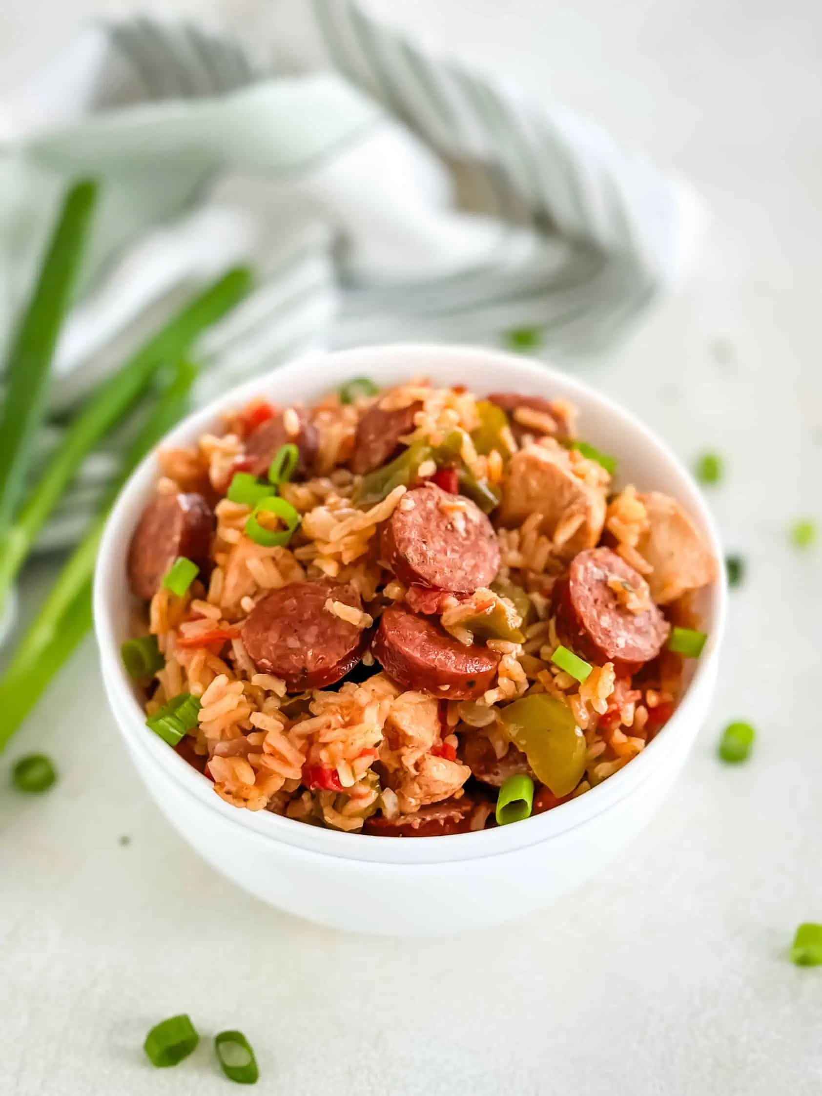 A bowl of flavorful rice mixed with sausage, chicken, and vegetables, garnished with fresh green onions.