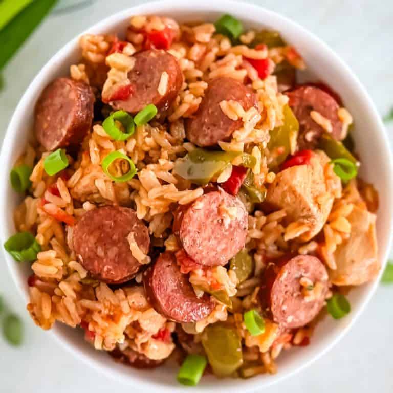 A zoomed-in shot of a savory rice and sausage meal, topped with fresh green onions and served in a white bowl.