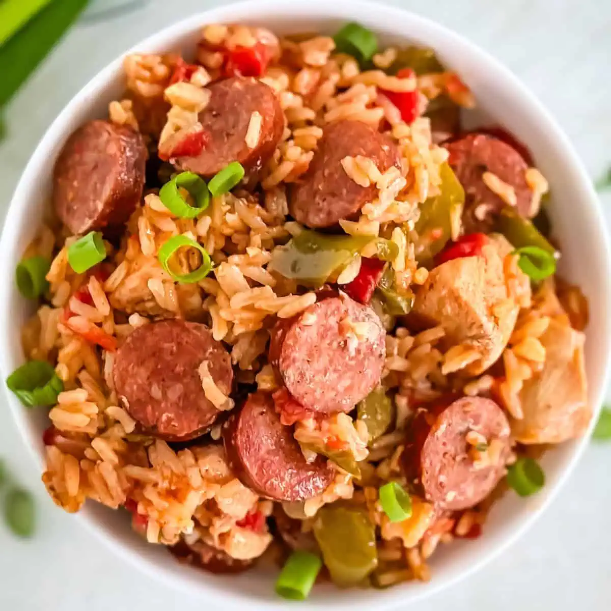 A zoomed-in shot of a savory rice and sausage meal, topped with fresh green onions and served in a white bowl.