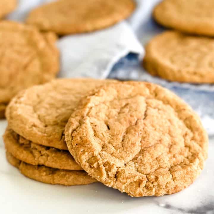 Close-up of three cinnamon cookies stacked on top of each other with more cookies in the background.