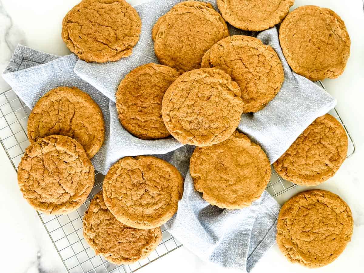 A batch of golden-brown cinnamon cookies arranged on a cooling rack covered with a light blue cloth.