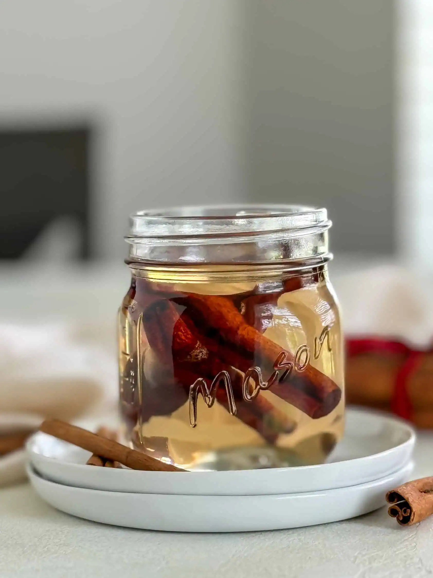 A mason jar filled with homemade cinnamon syrup, placed on a white plate.