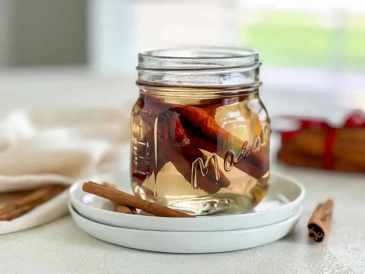 Side view of a mason jar filled with syrup, highlighting the rich amber color of the liquid and the cinnamon sticks inside.