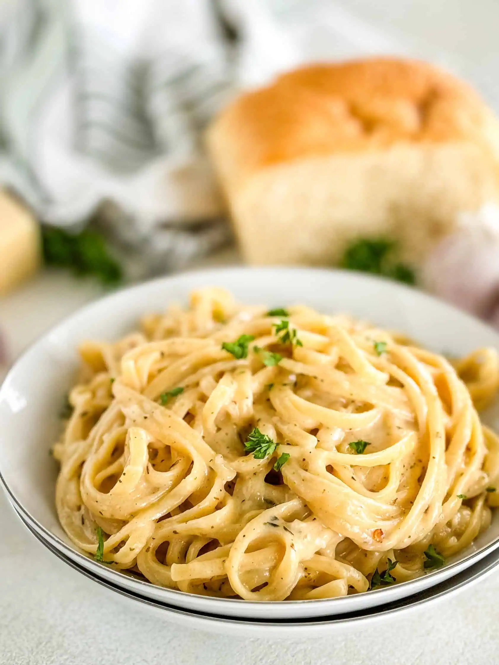 A bowl of creamy pasta with garlic cloves and bread in the background.