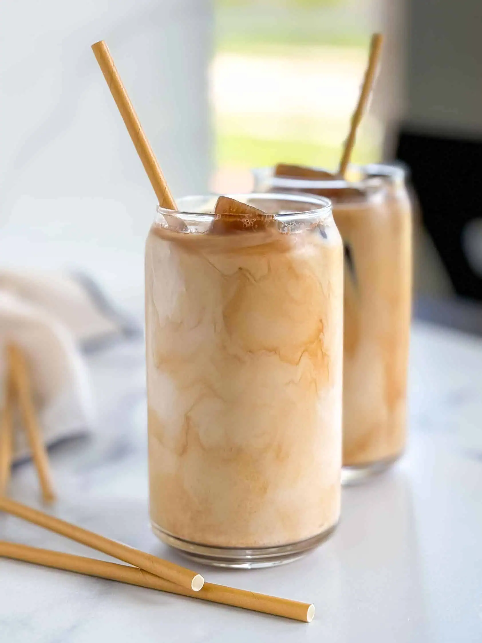 Two glasses of iced coffee with bamboo straws, showcasing the creamy swirls and ice cubes.