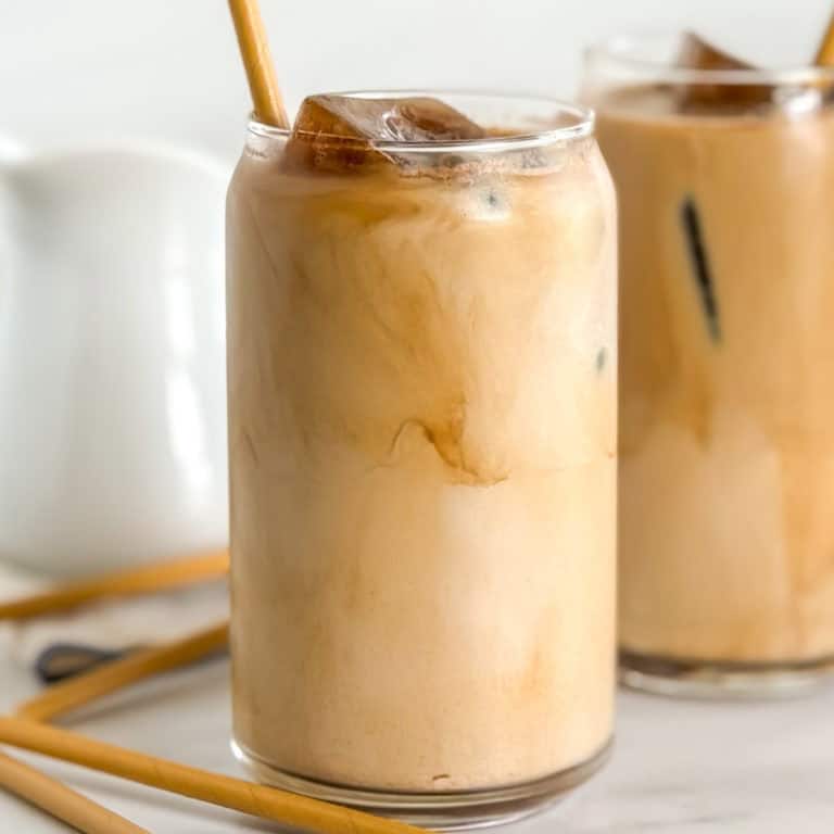 Close-up of a glass of iced coffee with a bamboo straw, showcasing a rich blend of coffee and cream.