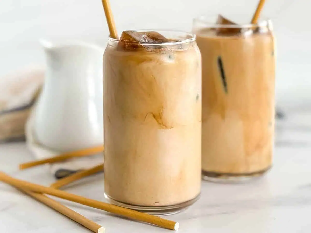 Two glasses of iced coffee with bamboo straws and ice cubes, sitting on a marble surface.