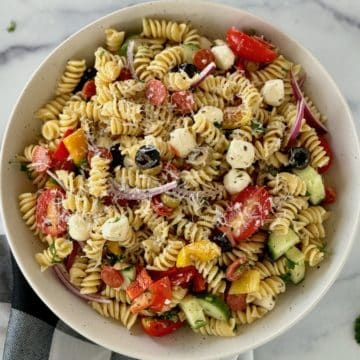 A bowl of vibrant pasta dish with rotini pasta, colorful veggies, creamy cheese, and a zesty dressing, garnished with fresh herbs.