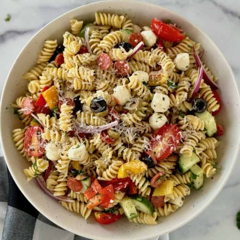 A bowl of vibrant pasta dish with rotini pasta, colorful veggies, creamy cheese, and a zesty dressing, garnished with fresh herbs.