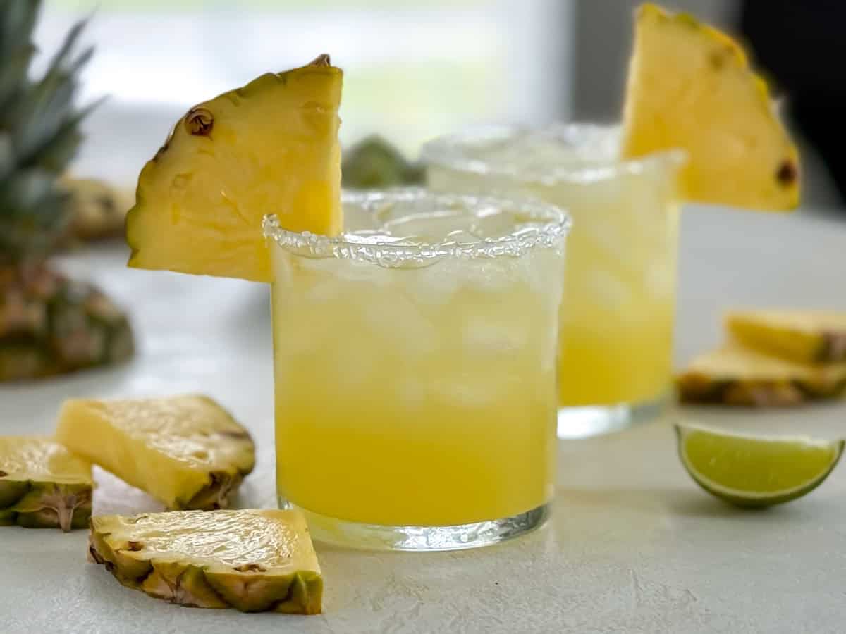 Close-up of a cocktail showing the textured salted rim and a juicy pineapple garnish.