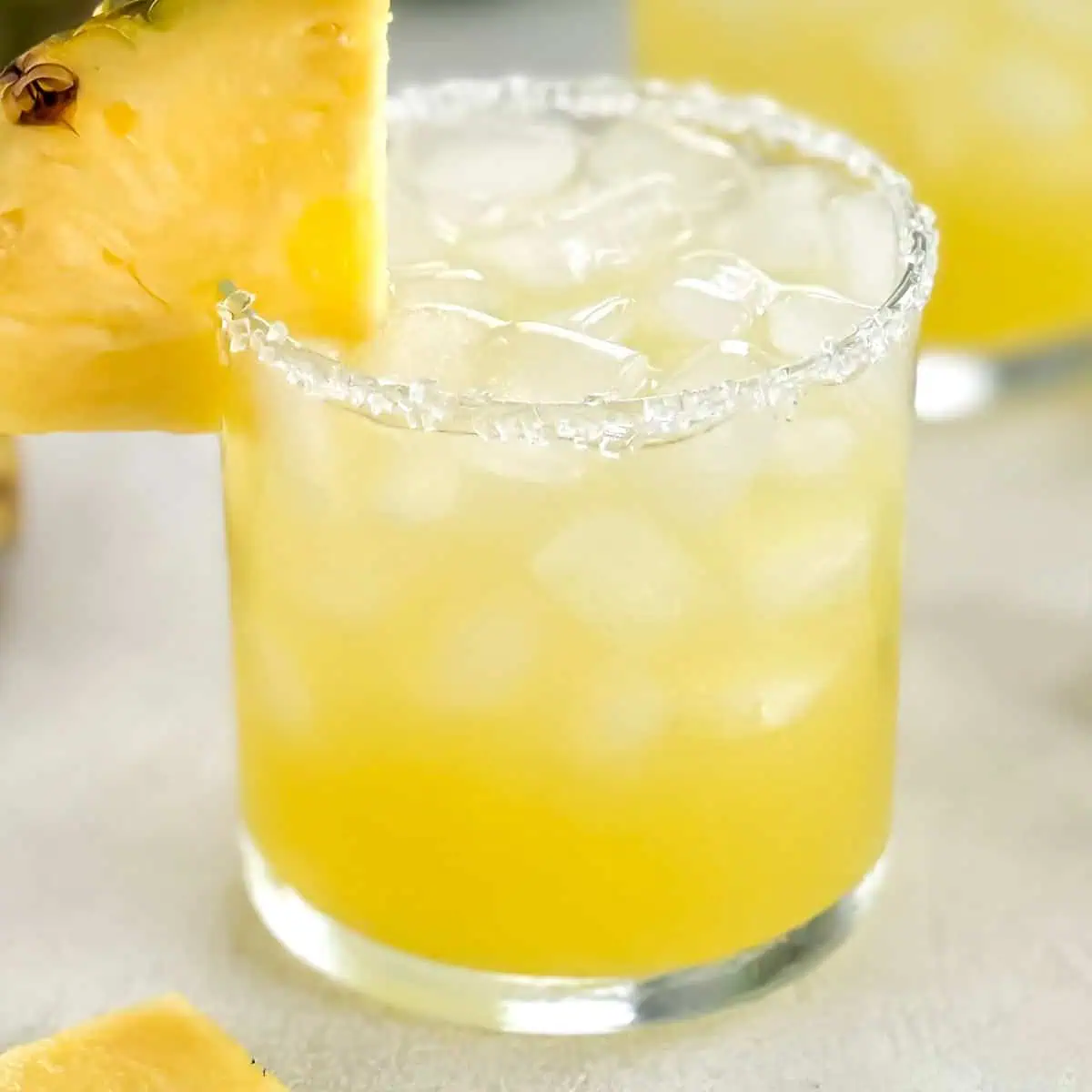 Refreshing yellow cocktail with a slice of pineapple on the rim and a textured salted rim.