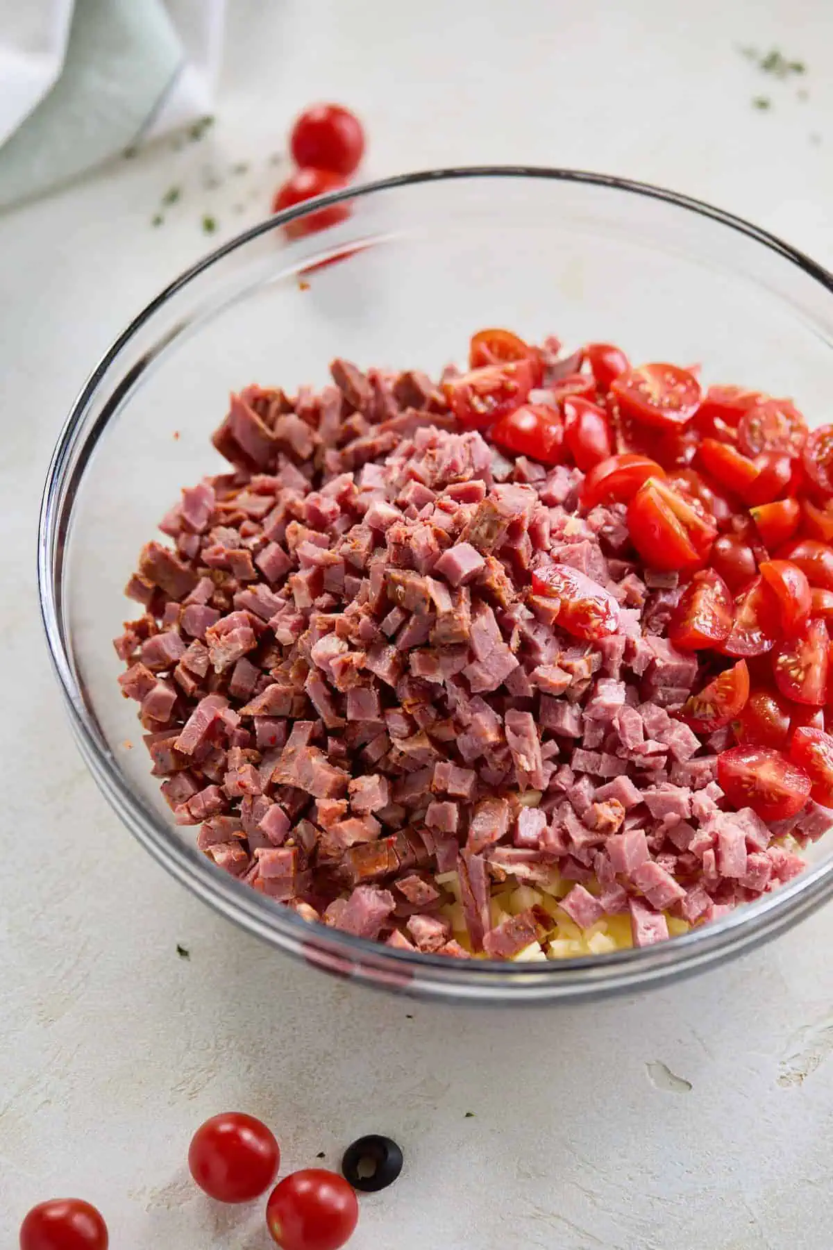 A large glass bowl filled with diced italian meats including salami, pepperoni, and capicola, along with quartered cherry tomatoes.