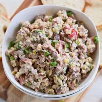 A top-down view of the hoagie dip in a white bowl, highlighting the colorful mixture of ingredients and garnished with green onions, with baguette slices on the side.