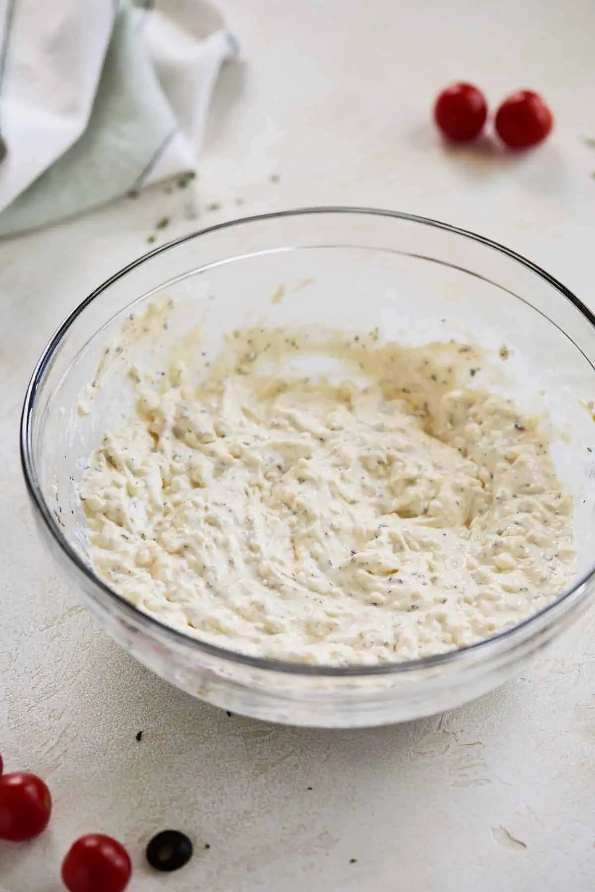 A large glass bowl containing a creamy mixture of mayonnaise, cream cheese, italian dressing, and spices.