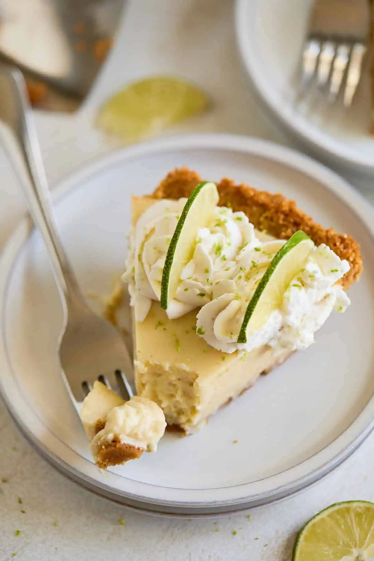 A slice of key lime pie on a white plate, with a bite taken out and a fork beside it.