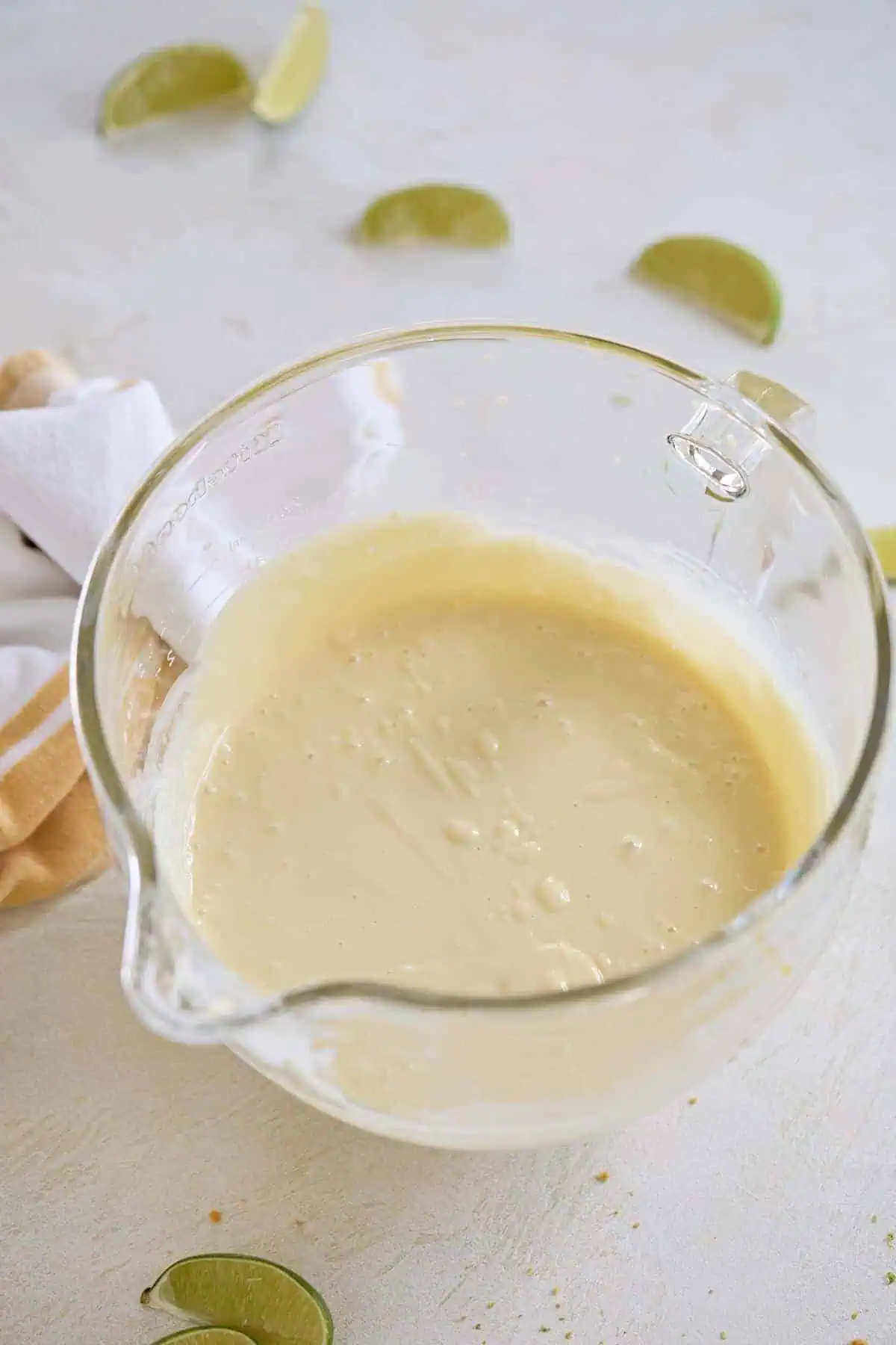 Pie filling mixture in a clear glass mixing bowl with lime slices in the background.