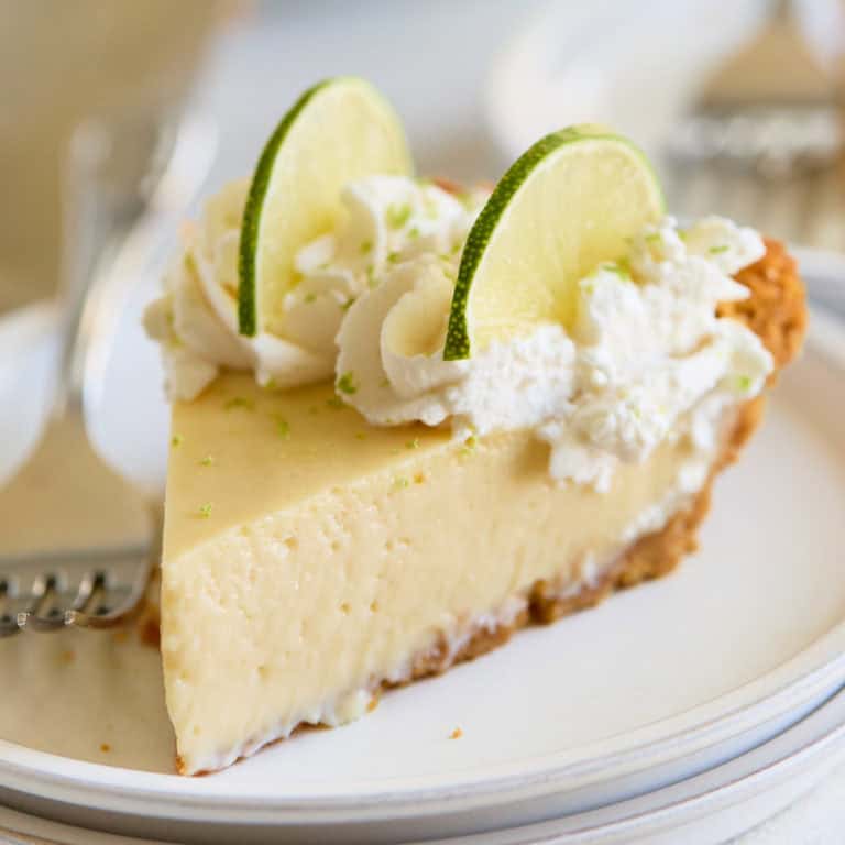 A close-up slice of creamy key lime pie topped with whipped cream and lime slices on a white plate.