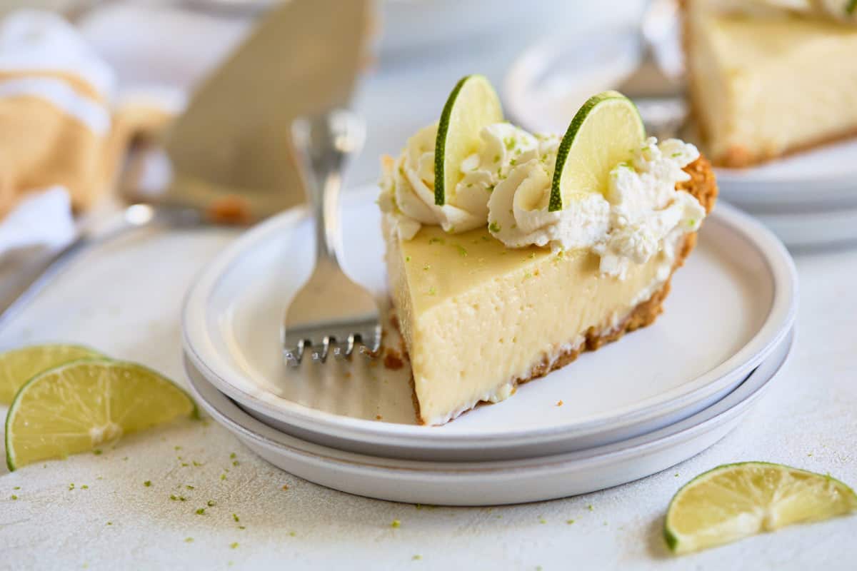 A slice of pie with whipped cream and lime slices, served on a white plate with a fork.