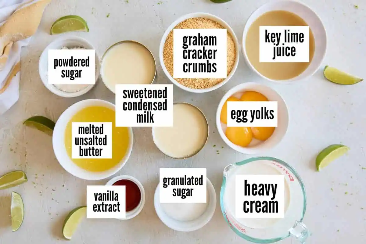 Ingredients for key lime pie arranged on a white surface, including graham cracker crumbs, egg yolks, and sweetened condensed milk.