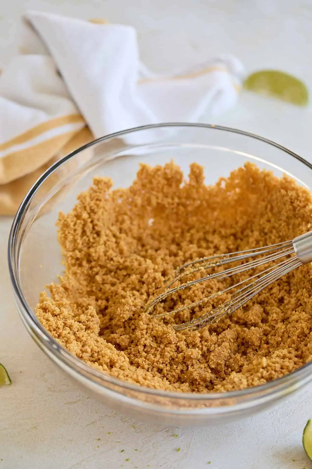 A clear glass mixing bowl filled with graham cracker crust mixture being whisked.