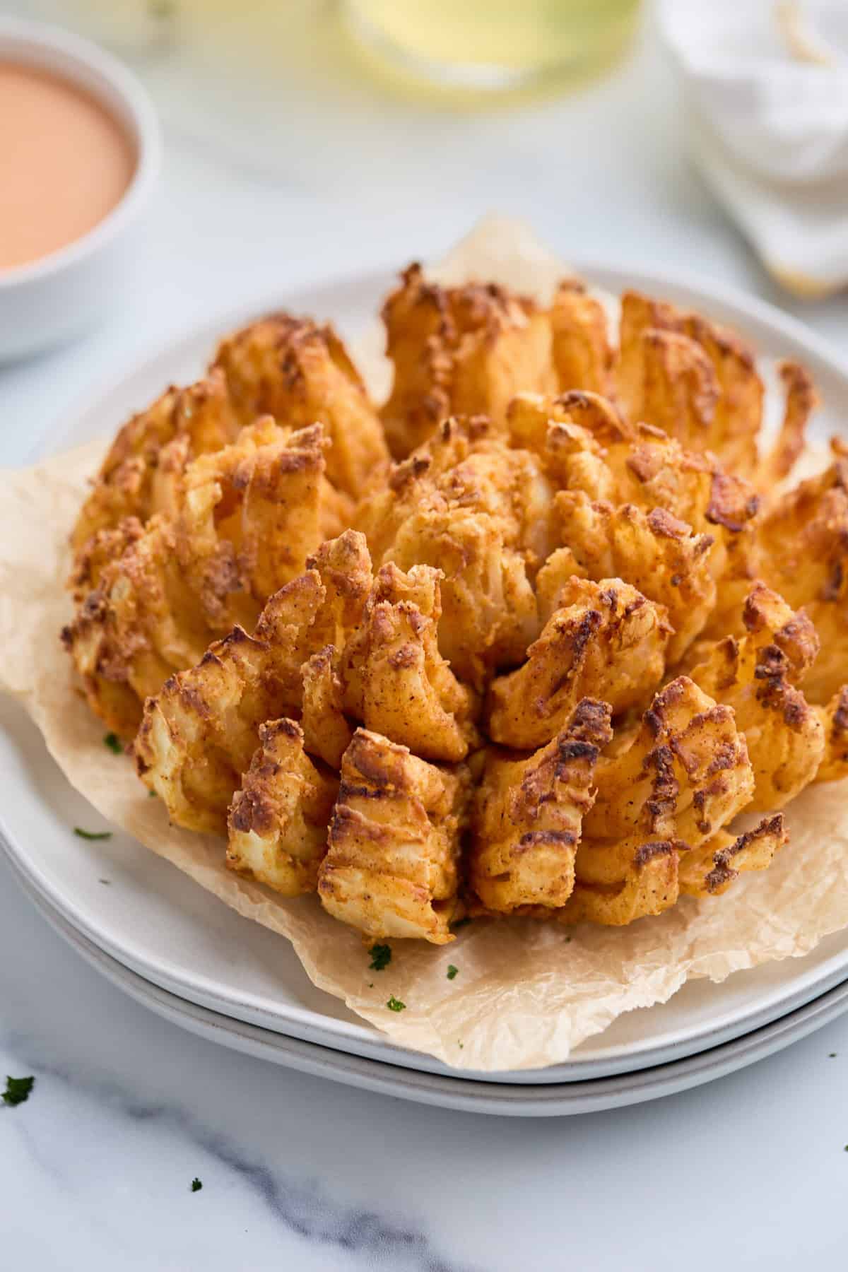 Air fryer blooming onion on parchment paper with dipping sauce in the background.