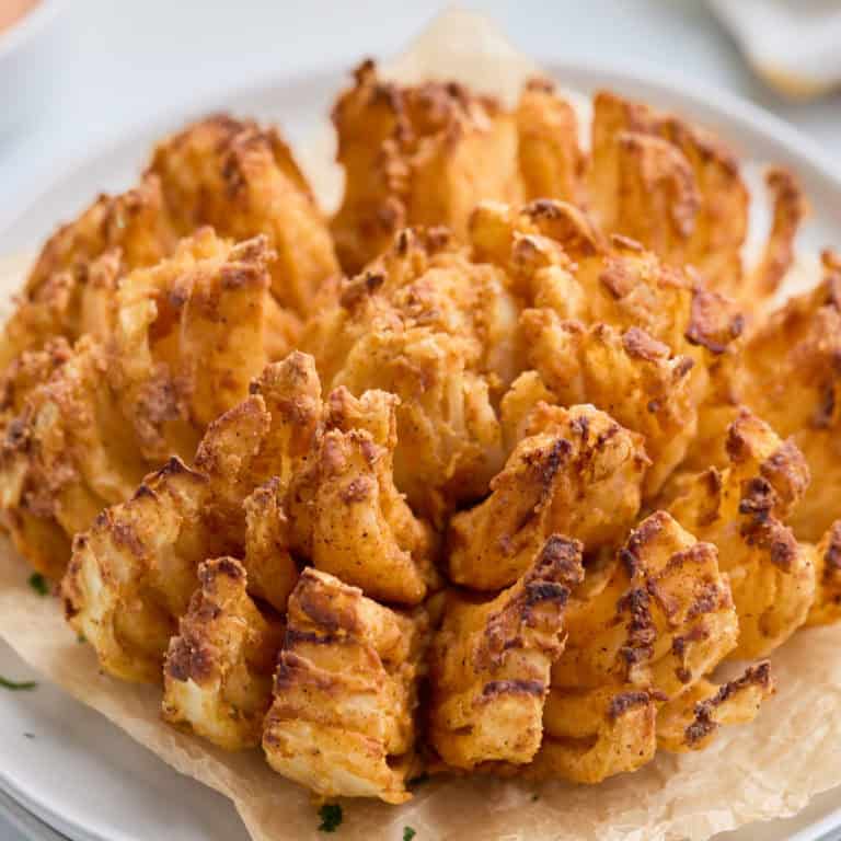 Close-up of a perfectly crispy air fryer blooming onion on a white plate.