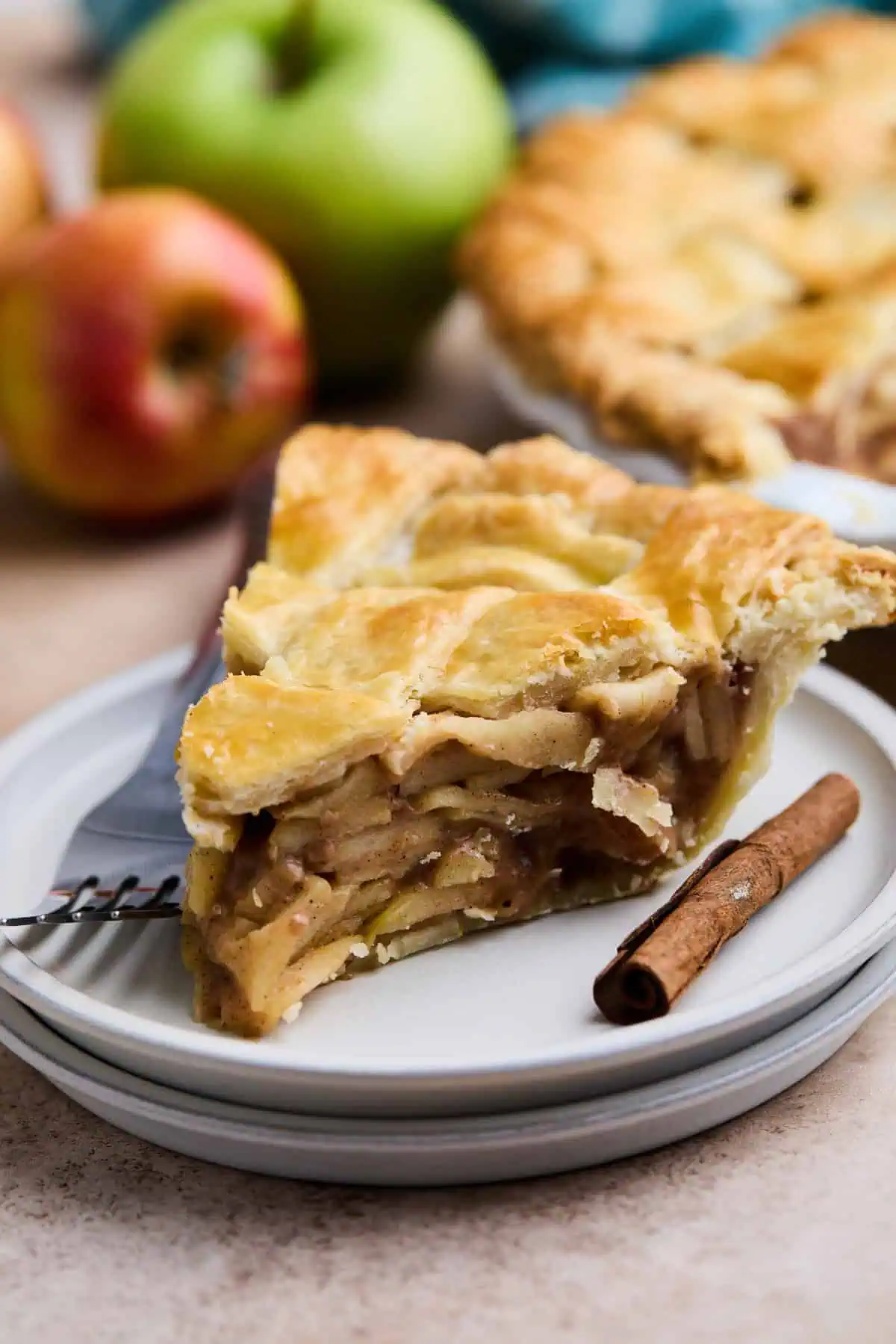 A close-up of a slice of apple pie, focusing on the thick, layered apple filling and golden, flaky crust.