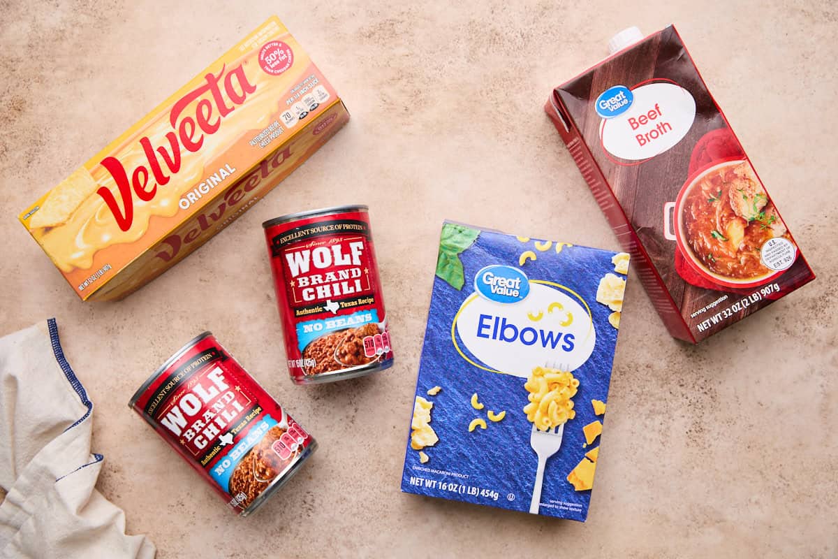 Ingredients laid out for making chili mac, including velveeta, canned chili, elbow macaroni, and beef broth