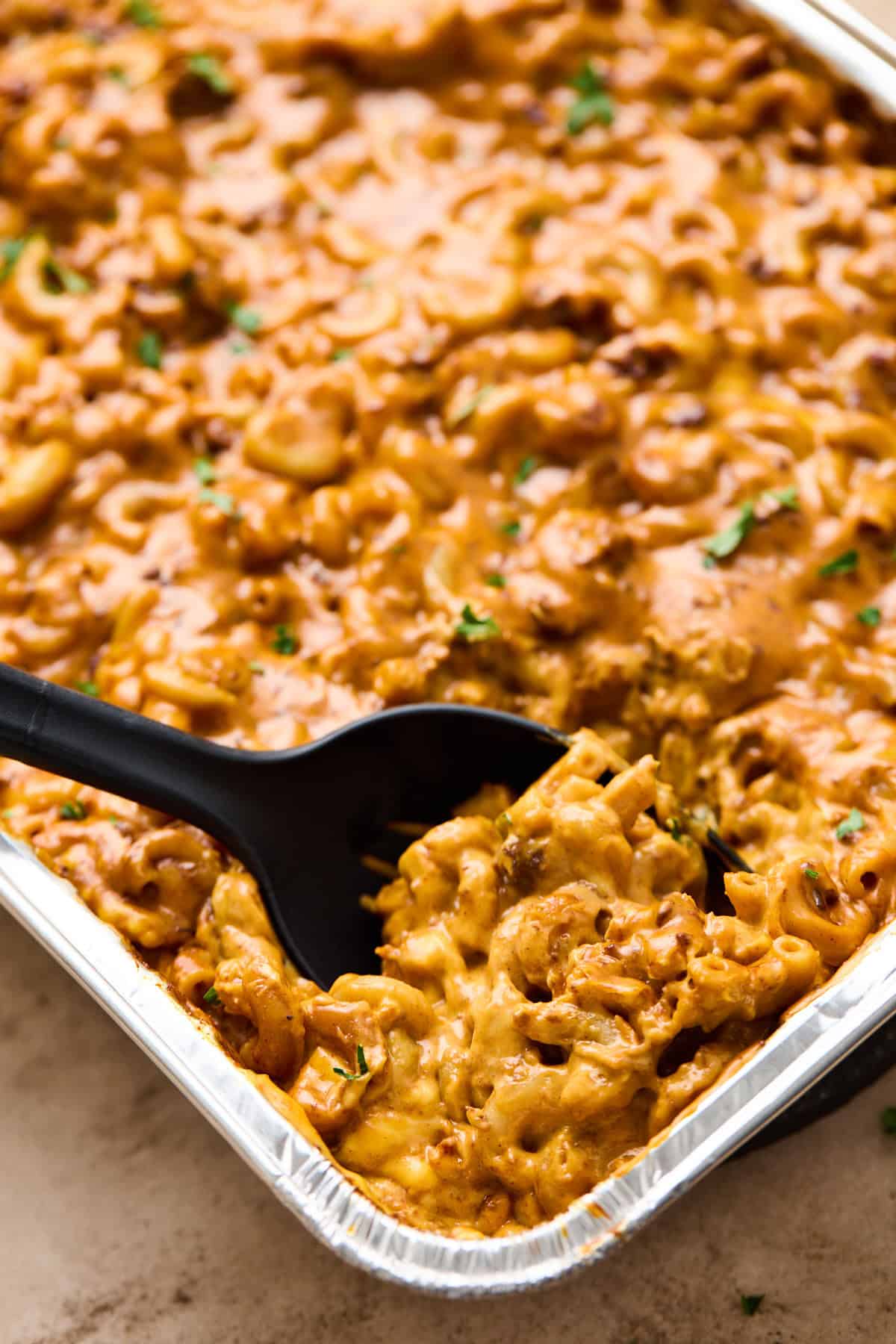 A spoonful of cheesy chili mac being served from a pan.