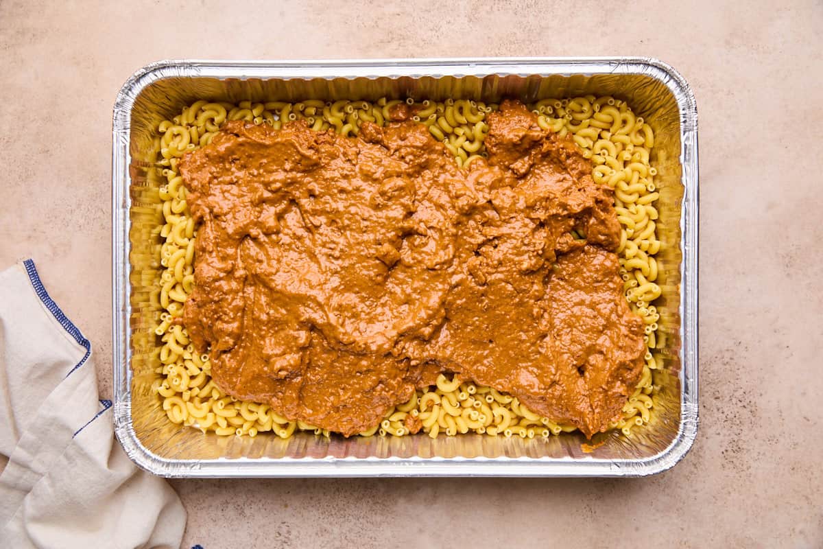 Canned chili spread over uncooked elbow macaroni in a baking dish