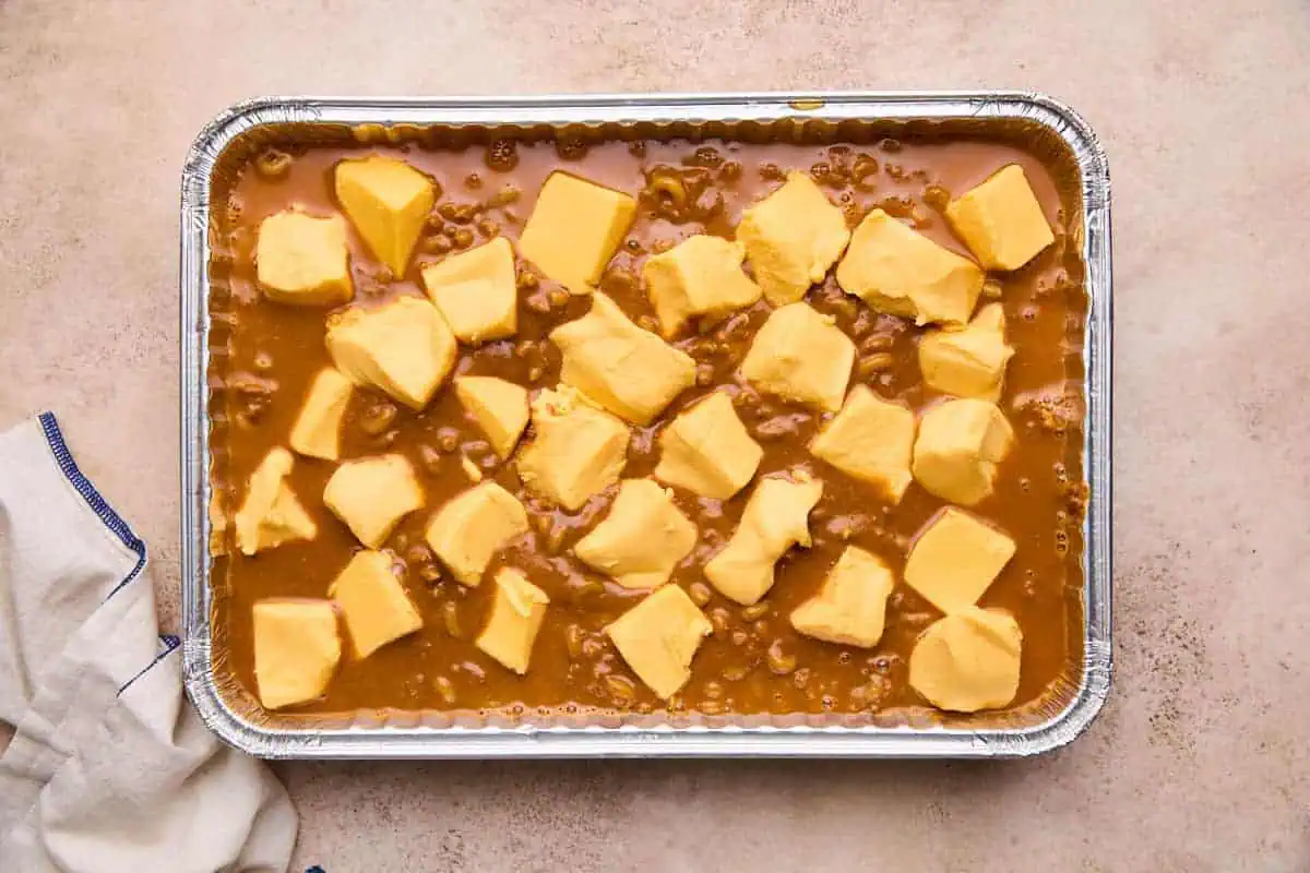 Cubes of velveeta cheese on top of chili and macaroni mixture in a baking dish.