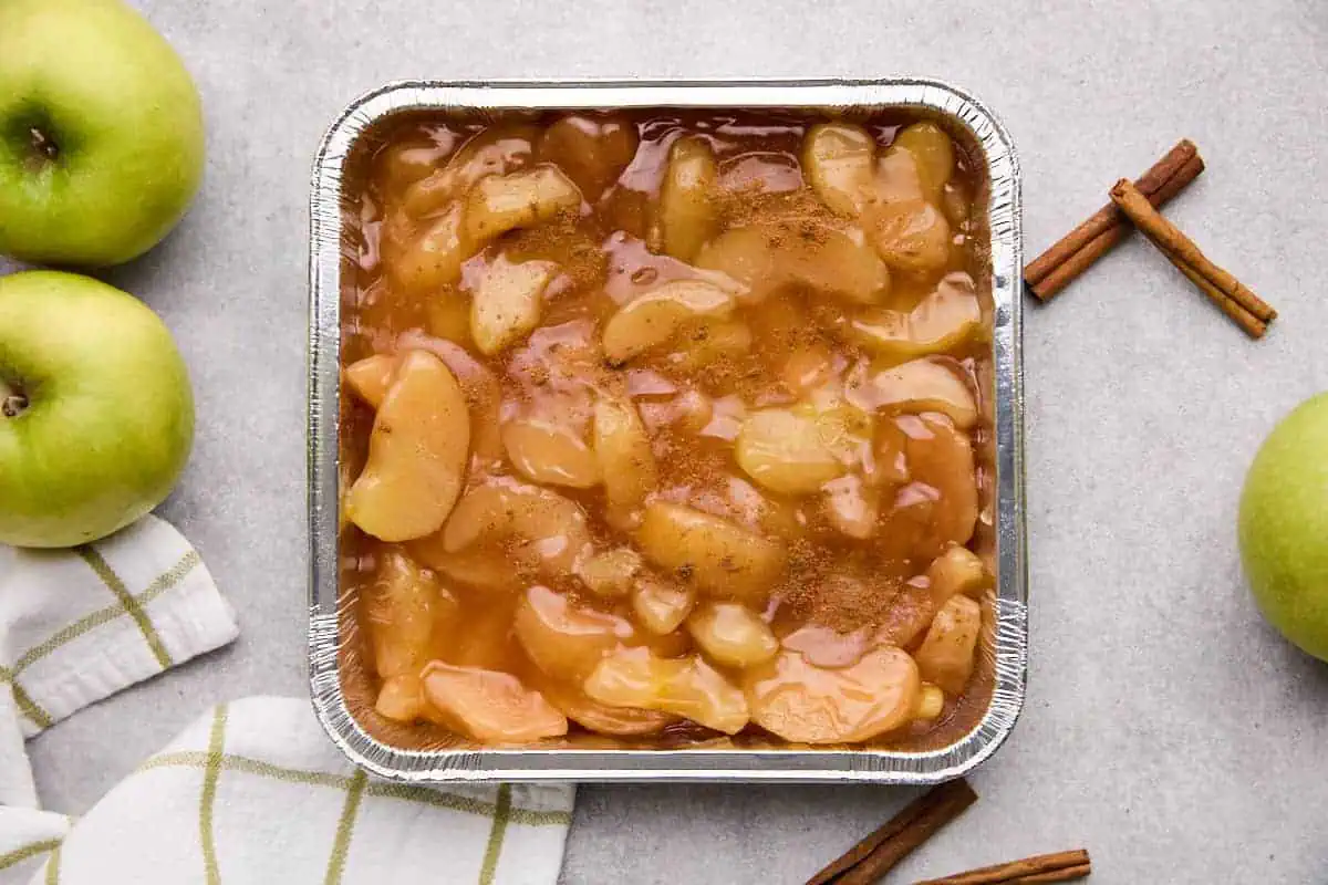 Apple pie filling dusted with apple pie spice in a baking dish for cinnamon roll cobbler.